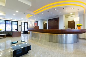 A modern reception area with a curved reception desk, a sofa, and a coffee table. - Sterling Hotel (Belgrade)