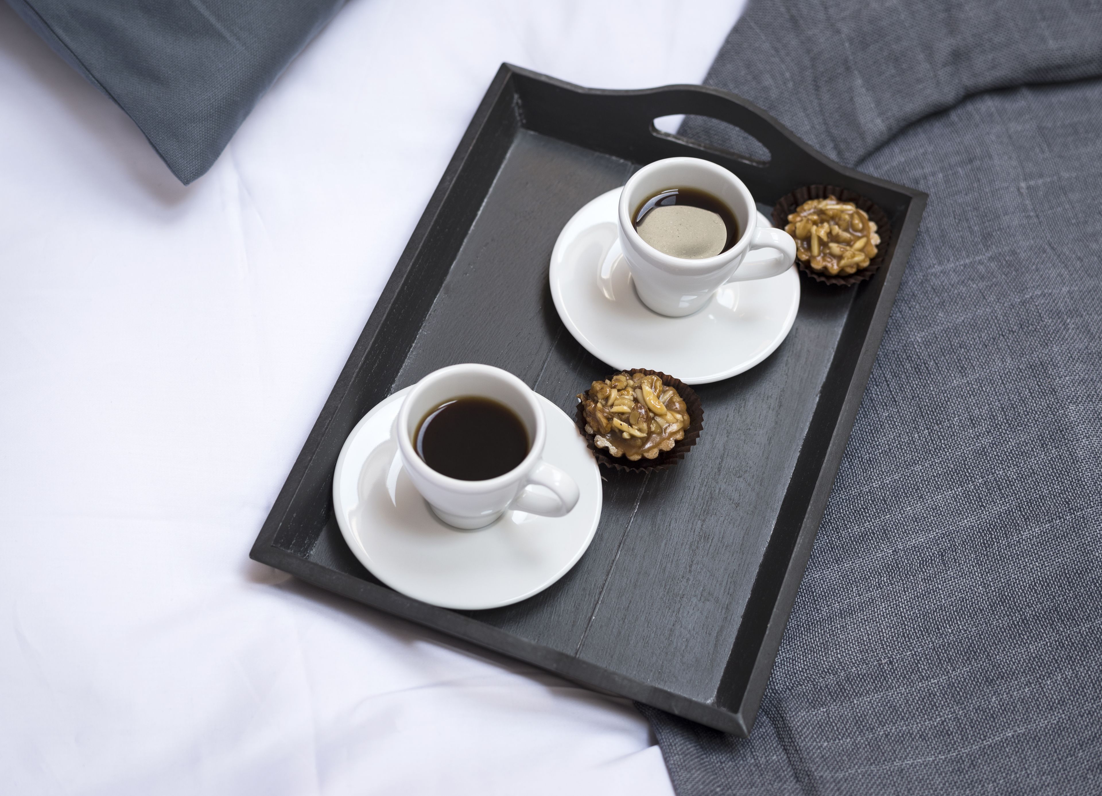 Ein Tablett mit zwei Kaffeetassen und zwei Gebäckstücken auf einem Bett.