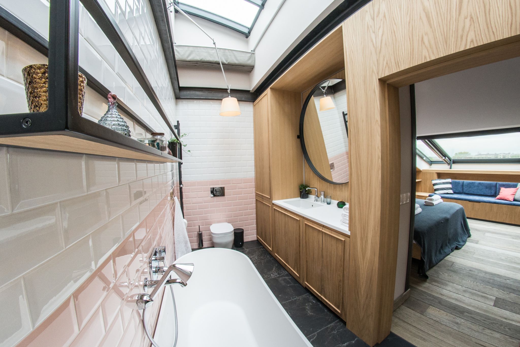 A modern bathroom with a large bathtub, wooden cabinets, a round mirror, and a skylight.