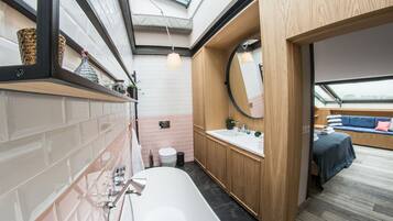 A modern bathroom with a large bathtub, wooden cabinets, a round mirror, and a skylight.