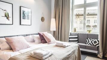 A hotel room with a bed, a sofa, a window with curtains, and artwork on the wall.