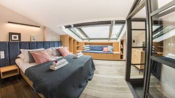 A modern bedroom with a skylight, a bed with pillows, a seating area, and a wooden desk.