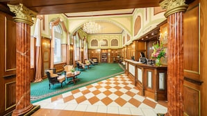 A lobby with a checkered floor, wooden columns, chandeliers, and a reception desk. - Hotel Bellevue Vienna (Vienna)