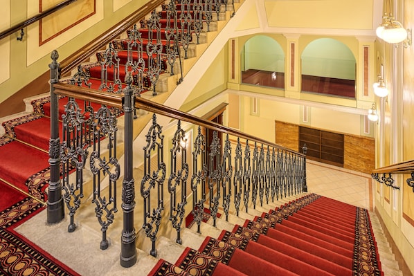Un magnifique escalier, orné de rampes en fer forgé et dont les marches sont recouvertes d’un tapis rouge, mène à l’étage supérieur.