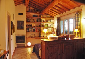 A cozy room with a fireplace, wooden shelves with books, and two lamps on a wooden table.