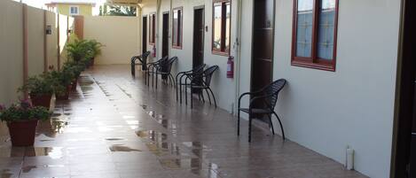 A corridor with tiled flooring, potted plants, and chairs along the walls.
