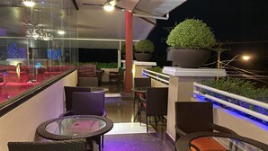 Een balkon buiten met rieten meubels, een glazen tafel en een bloempot.