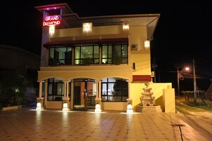 A hotel with a prominent sign reading "Grand Diamond Hotel," featuring a two-story structure with large windows and a central entrance.