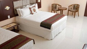 Een hotelkamer met een groot bed, twee stoelen, een klein tafeltje en een nachtkastje.