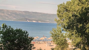 Una playa con sombrillas y sillas de descanso, vista despejada al mar y montañas a lo lejos.