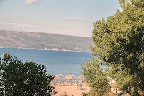 A beach with umbrellas and lounge chairs, a clear view of the sea, and distant mountains. - Cavos Beach House (Corfu)