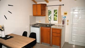 A compact kitchen with wooden cabinets, a white dishwasher, and a small dining area with a wooden table and black chairs.