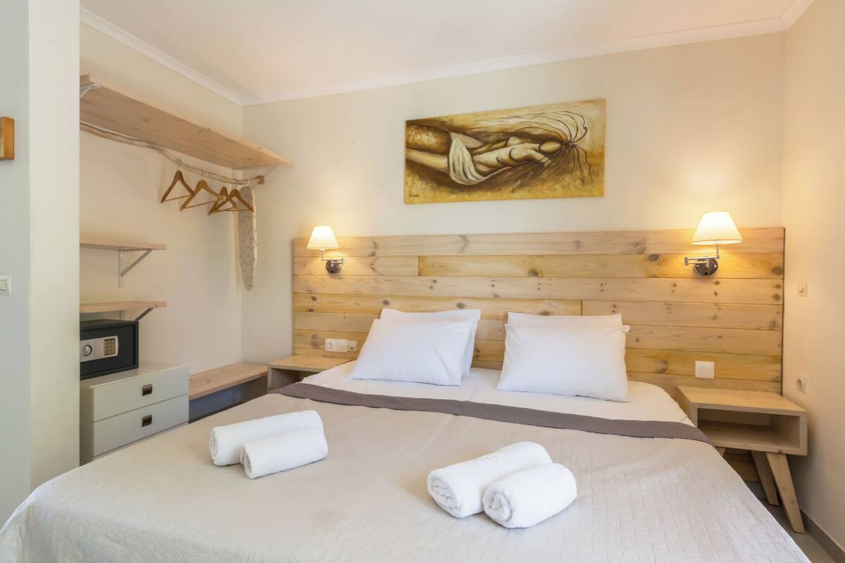 A hotel room with a wooden headboard, two bedside tables, a bed with white linens, and a painting on the wall.