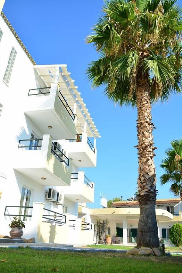 A multi-story building with balconies, a palm tree in front, and a clear blue sky. - Cavos Beach House (Corfu)