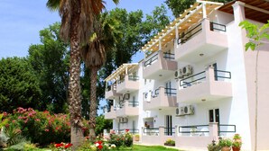 A multi-story building with balconies, air conditioning units, and a garden with various plants and flowers. - Cavos Beach House (Corfu)