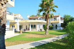 A multi-story building with a covered patio area, palm trees, and a well-maintained lawn. - Cavos Beach House (Corfu)