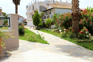 A pathway leading to a modern building with a balcony, surrounded by lush greenery and flowering plants. - Cavos Beach House (Corfu)