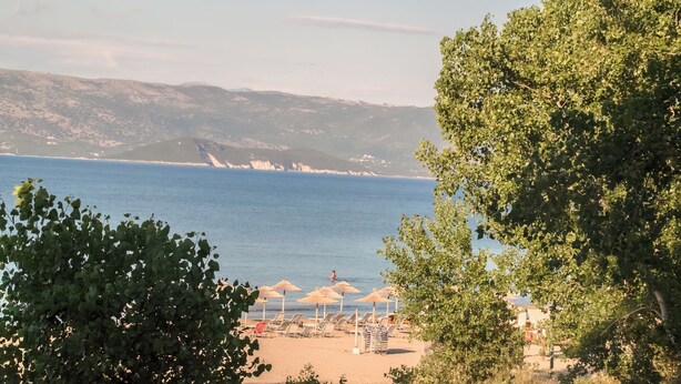 A beach with umbrellas and lounge chairs, a clear view of the sea, and distant mountains. - Cavos Beach House (Corfu)
