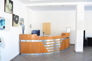 A reception desk with a wooden finish, a computer monitor, and a blue flower vase. - Cavos Beach House (Corfu)