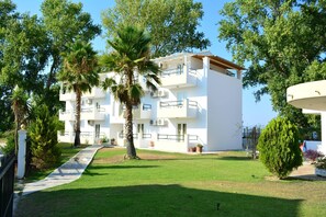 A modern multi-story building with balconies, surrounded by lush greenery and palm trees. - Cavos Beach House (Corfu)