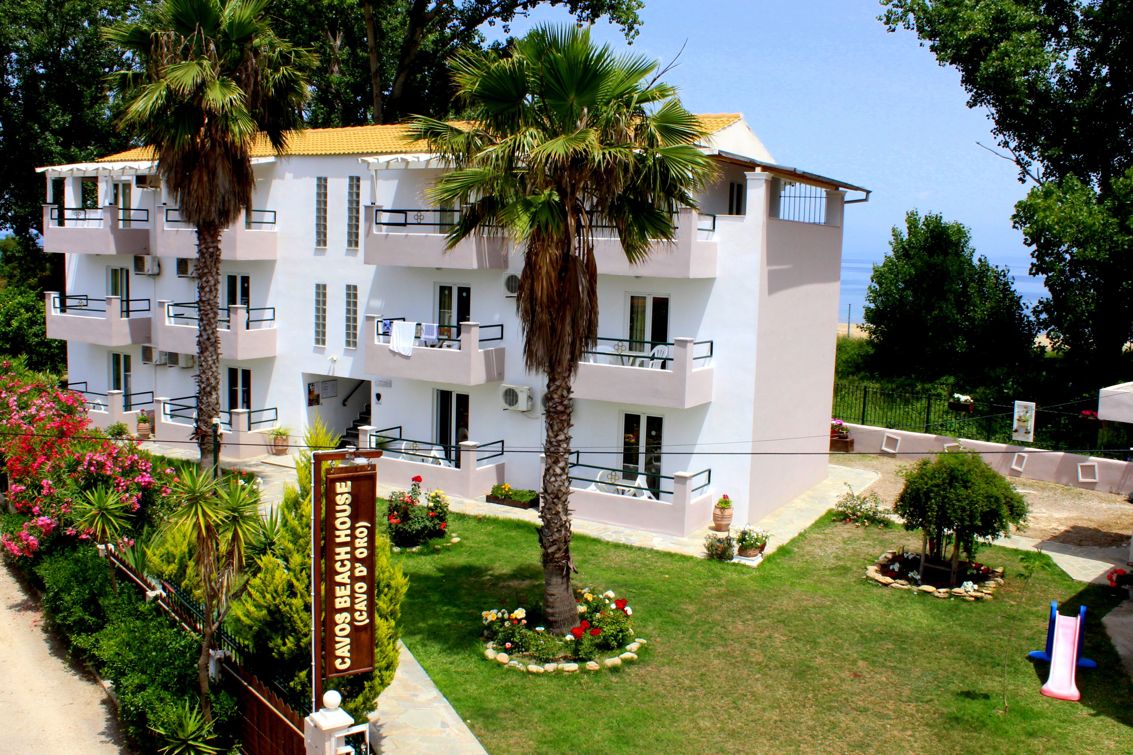 A multi-story hotel with balconies, a well-maintained lawn, and a palm tree.
