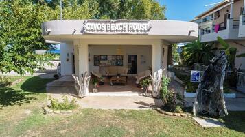 A beach house with a covered outdoor seating area, a sign reading "CAVOS BEACH HOUSE," and a sign requesting guests to wash their feet before entering.