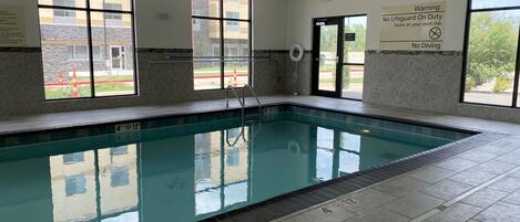 An indoor swimming pool with clear water, tiled walls, and large windows.