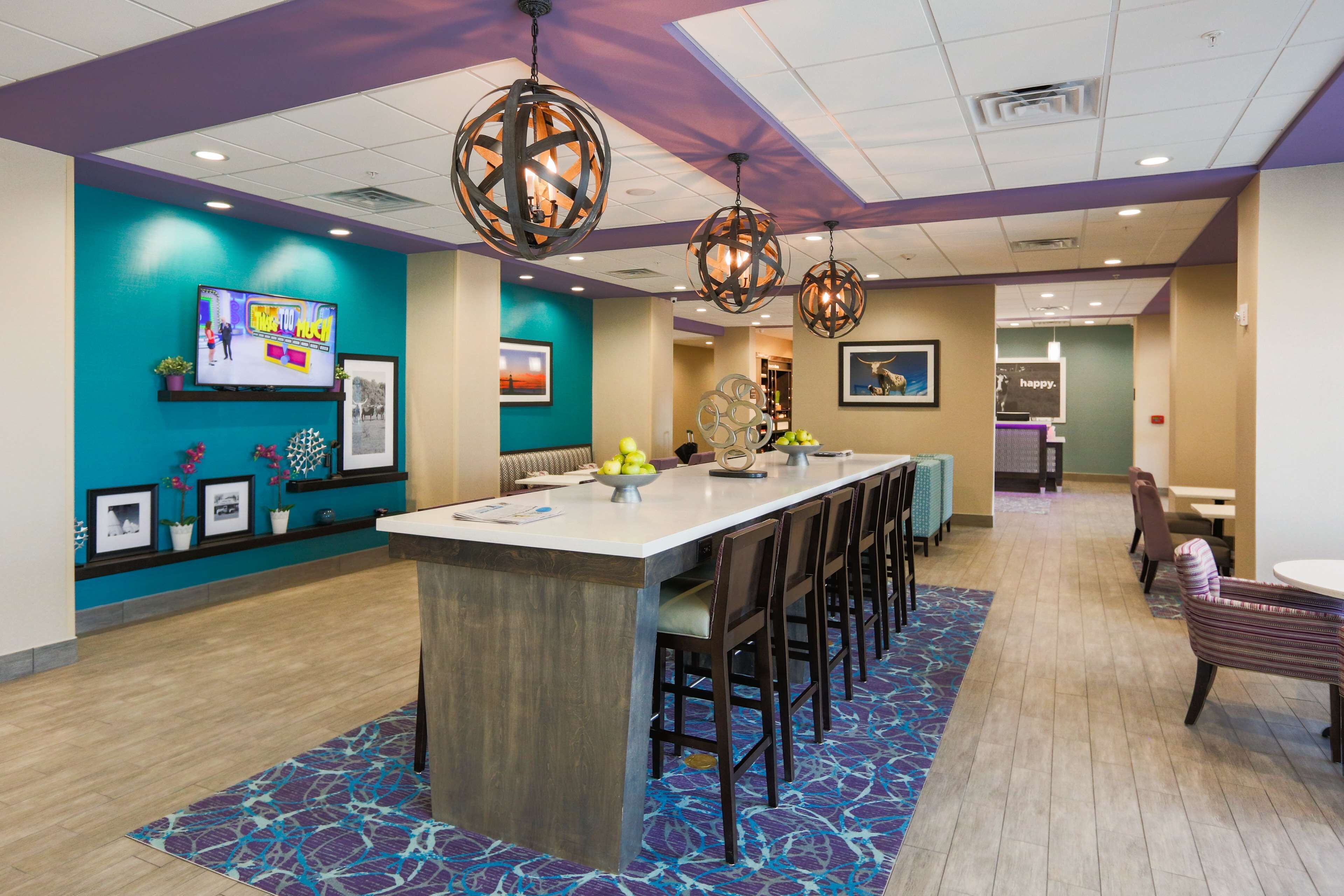A modern hotel lobby with a central bar area, seating arrangements, and decorative elements.