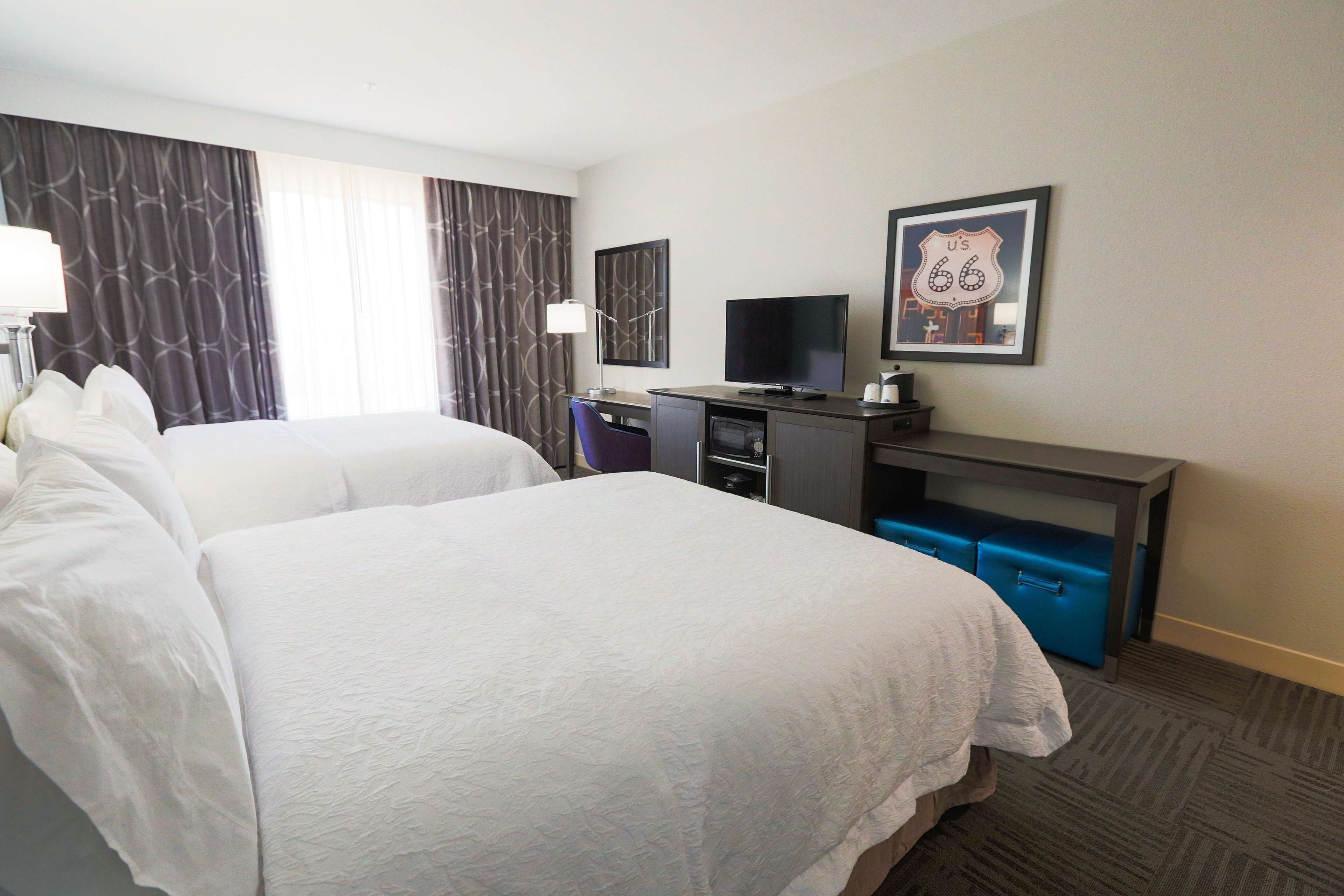 A hotel room with two beds, a desk with a TV, and a framed picture on the wall.