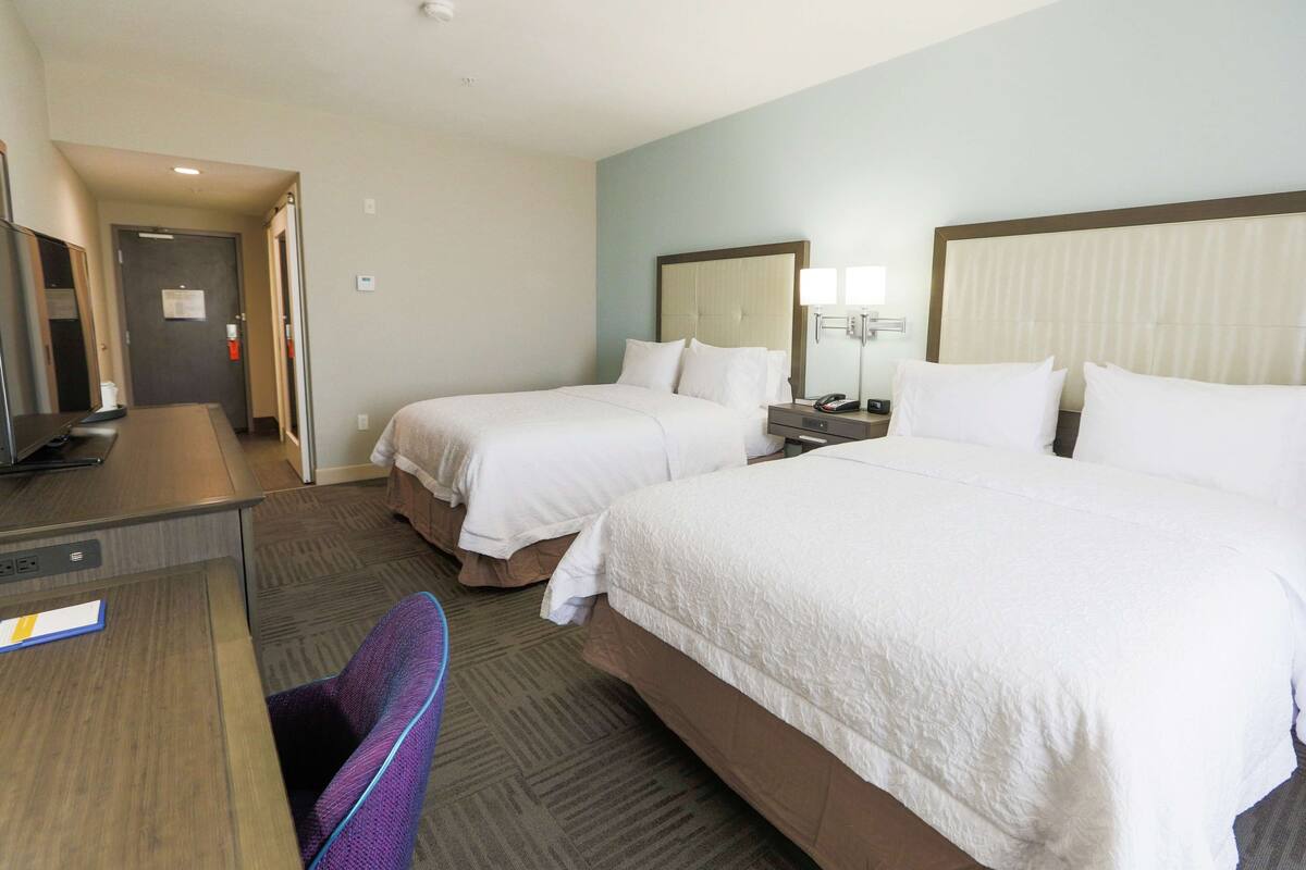 Ein Hotelzimmer mit zwei Betten, einem Schreibtisch, einem Stuhl und einem Fernseher.