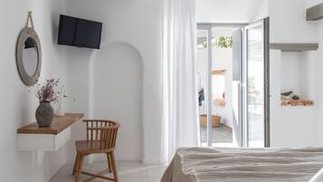 A bedroom with a bed, a wooden chair, a desk with a vase, a television, and a sliding glass door leading to an outdoor area.