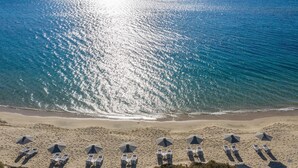 An aerial view of a beach with rows of sun loungers and umbrellas aligned along the shoreline. - Aqua Breeze Villas Naxos (Naxos)