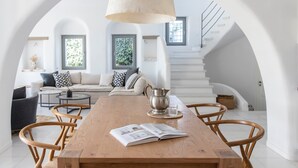 A spacious living room with a wooden dining table, a sofa set, and a staircase leading to an upper level. - Aqua Breeze Villas Naxos (Naxos)