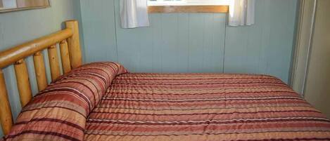 Een slaapkamer met een houten hoofdbord, een gestreept dekbed en een raam met gordijnen.