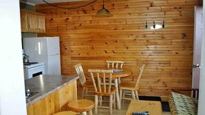 Cocina compacta con paneles de madera, un refrigerador blanco, una estufa y un comedor con sillas y mesa de madera.