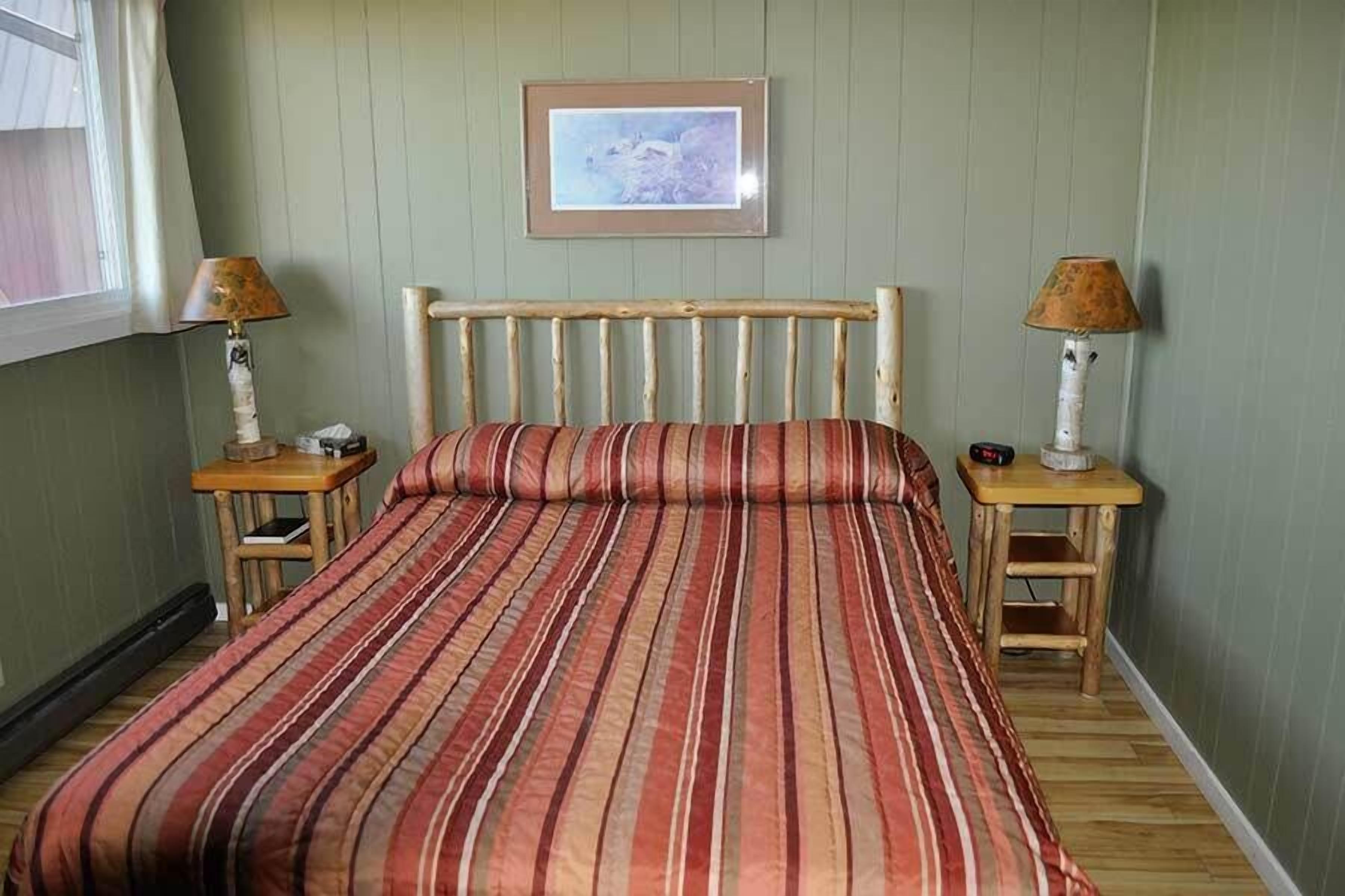 A room with a bed, two nightstands, a framed picture on the wall, and a window.