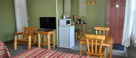 A room with a bed, two wooden chairs, a small table with a TV, a microwave, and a door with a number.