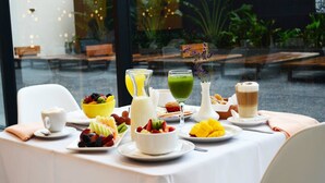 Ein Frühstückstisch mit verschiedenen Früchten, einer Kaffeetasse, einem Glas grüner Saft und einem Muffin.