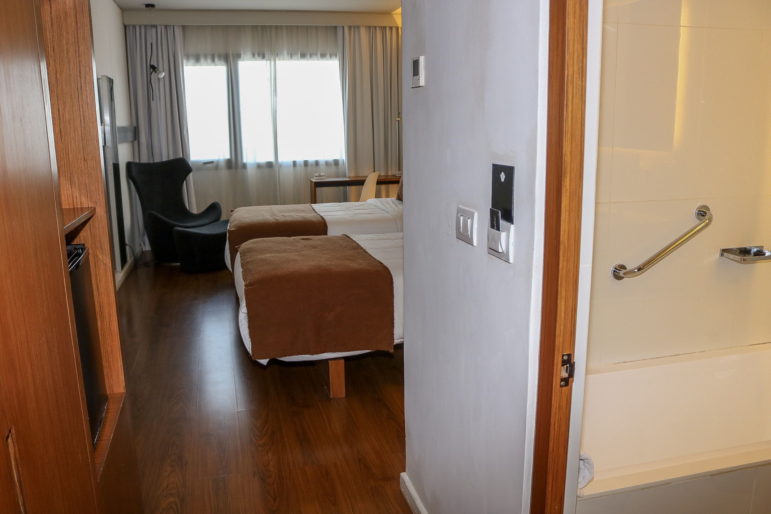 A hotel room with two beds, a desk, a chair, and a window with curtains.