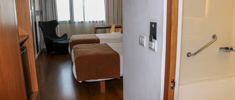 A hotel room with two beds, a desk, a chair, and a window with curtains.