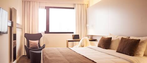 A hotel room with a large bed, a desk with a laptop, a chair, and a TV.