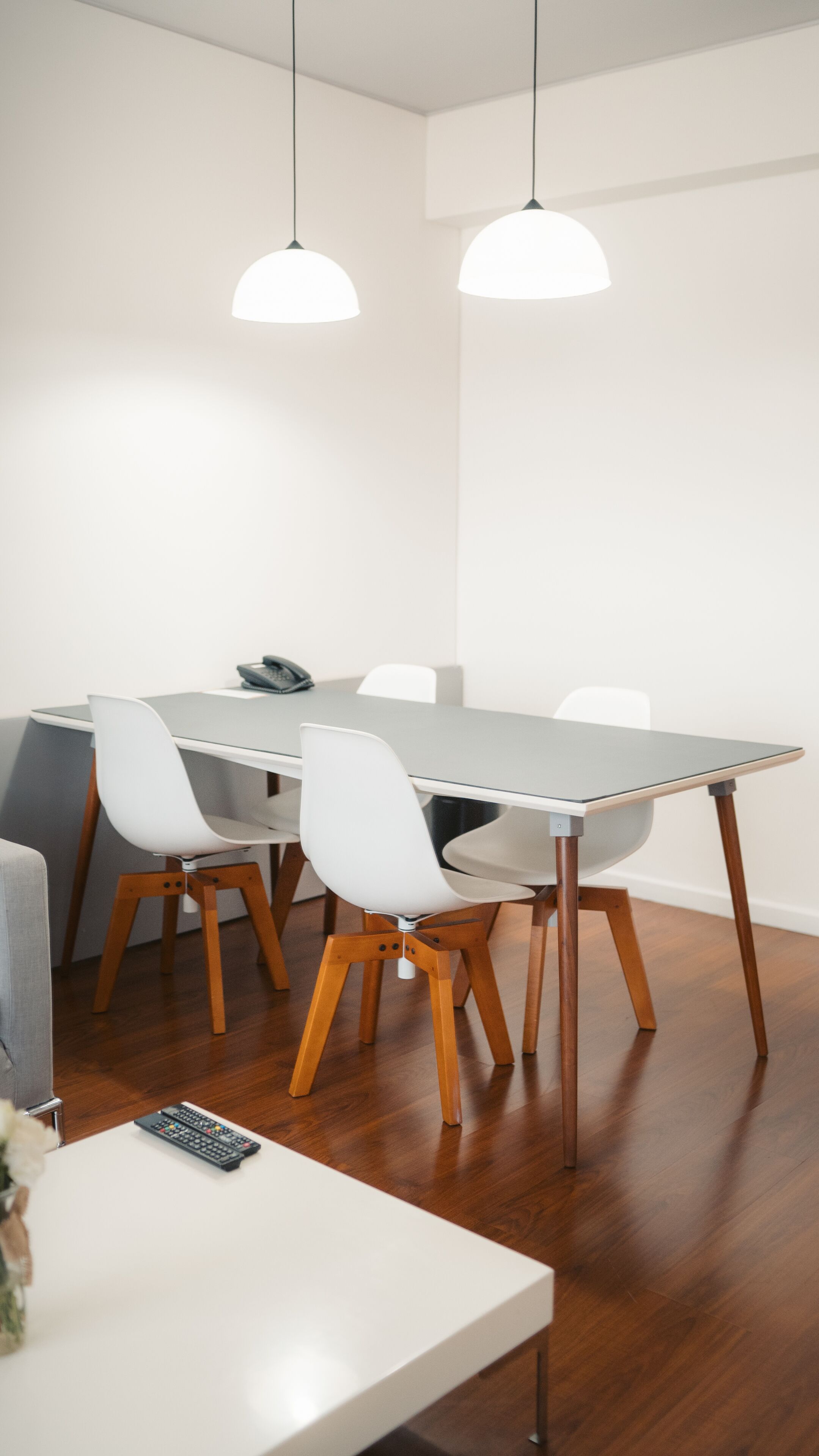Un comedor moderno con una mesa rectangular, sillas blancas y lámparas colgantes.