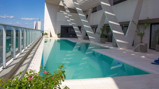 Ein moderner Poolbereich mit geometrischer Architektur, blauem Himmel und Blick auf die Stadt.