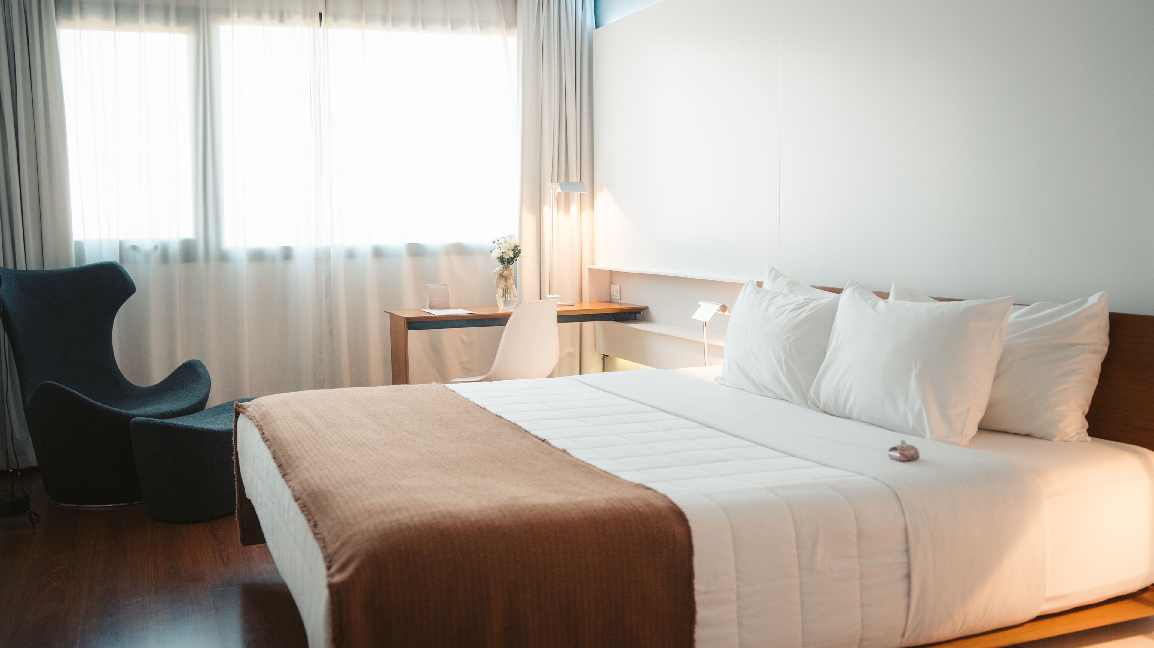 A hotel room with a bed, a chair, a desk, and a nightstand.