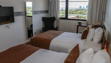Habitación de hotel con dos camas, televisión, silla, mesita y ventana con vista a la ciudad.