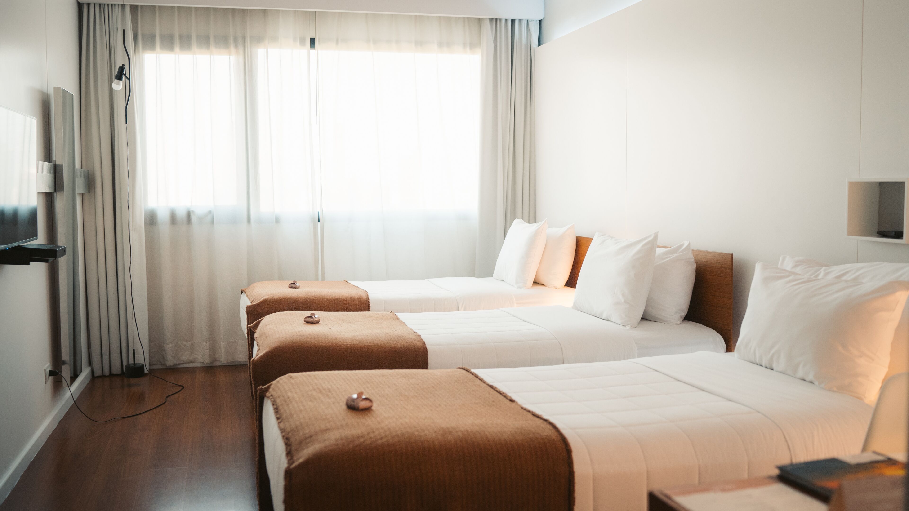 A hotel room with two beds, a TV, and a window with curtains.