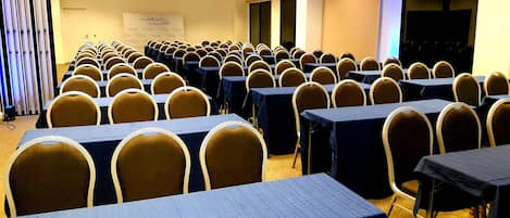 A conference room with rows of tables and chairs, a whiteboard, and a projection screen.