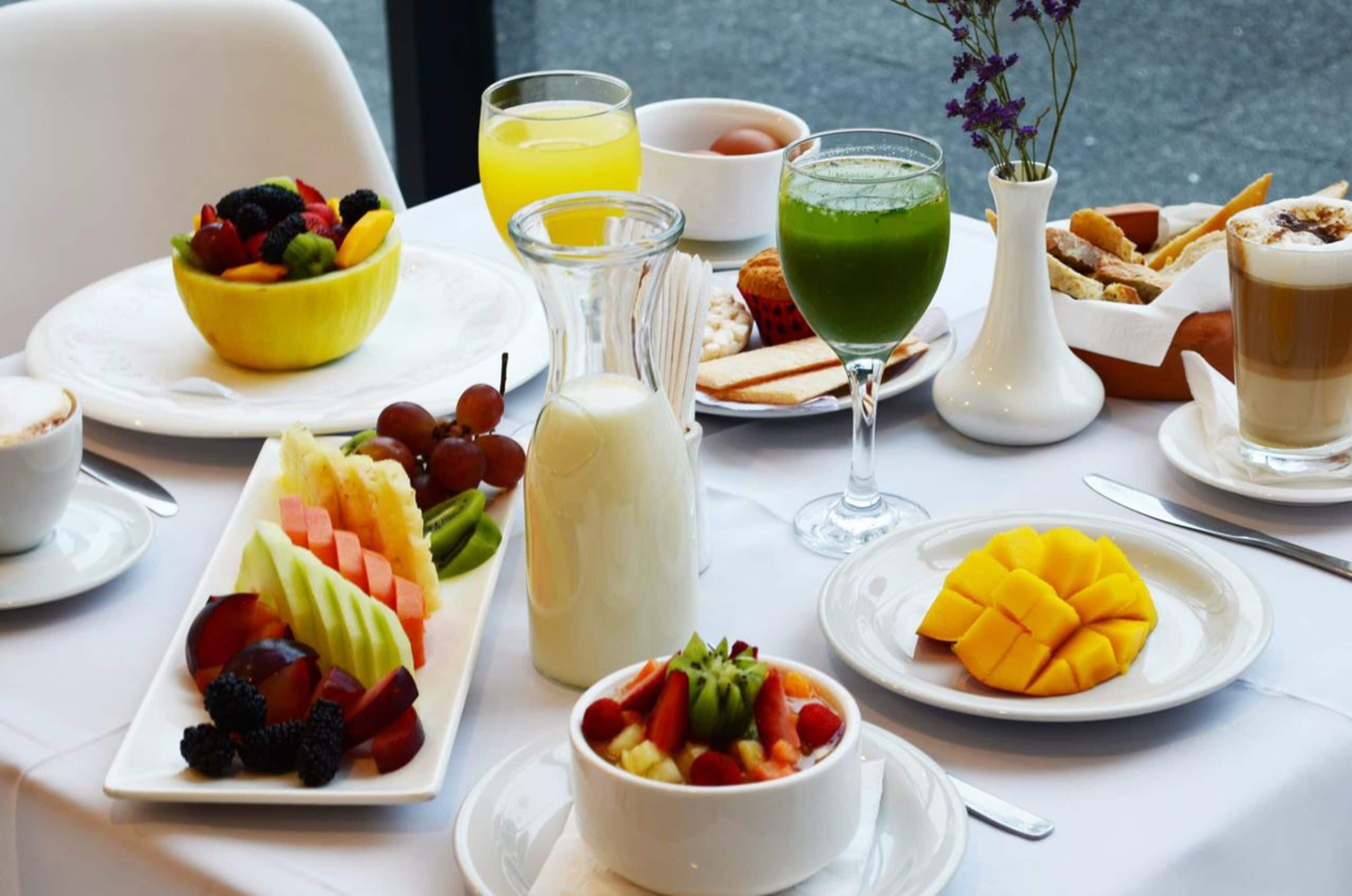 A breakfast setting with various fruits, beverages, and pastries on a table.