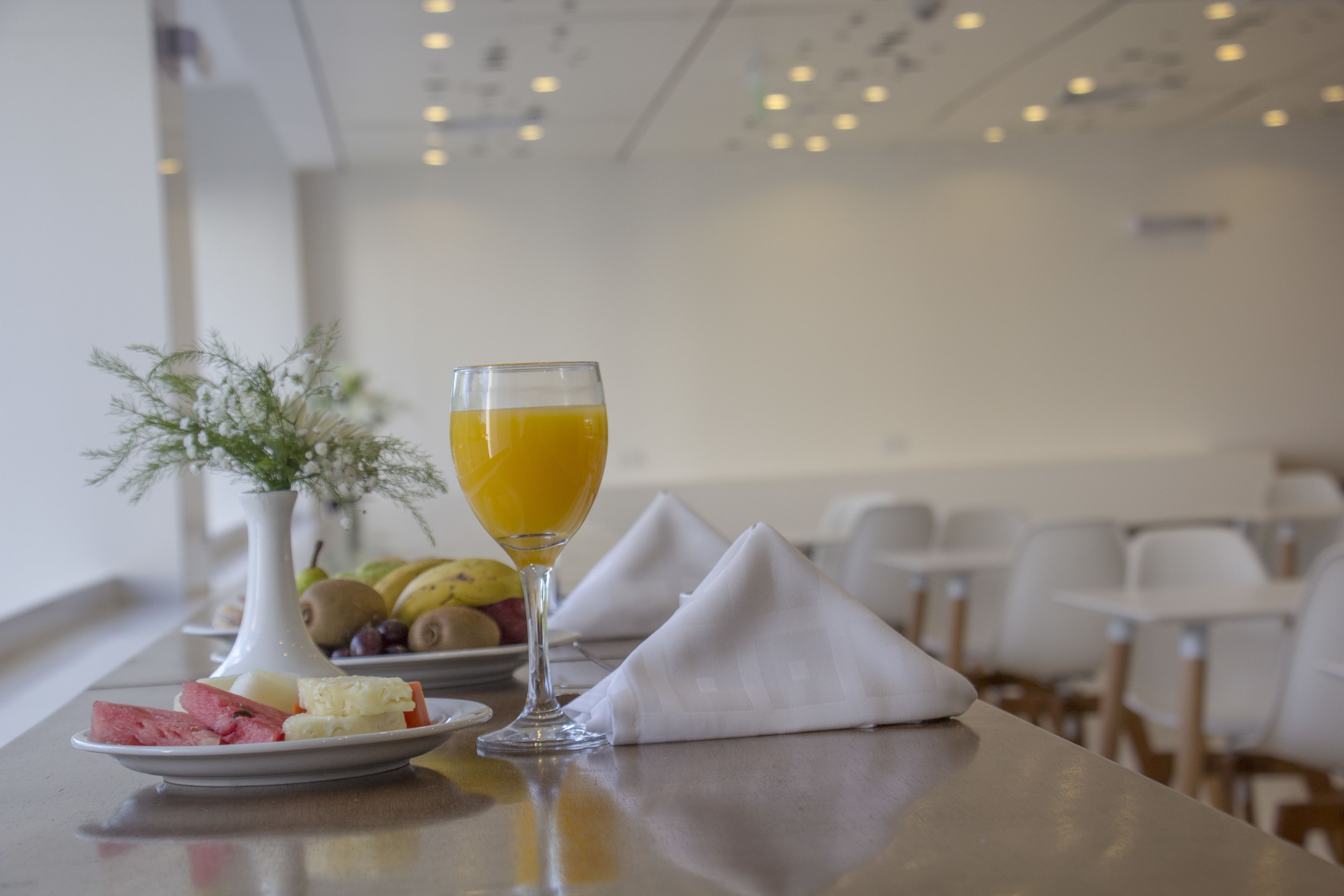 A dining table with a plate of assorted fruits, a glass of orange juice, and a white napkin.