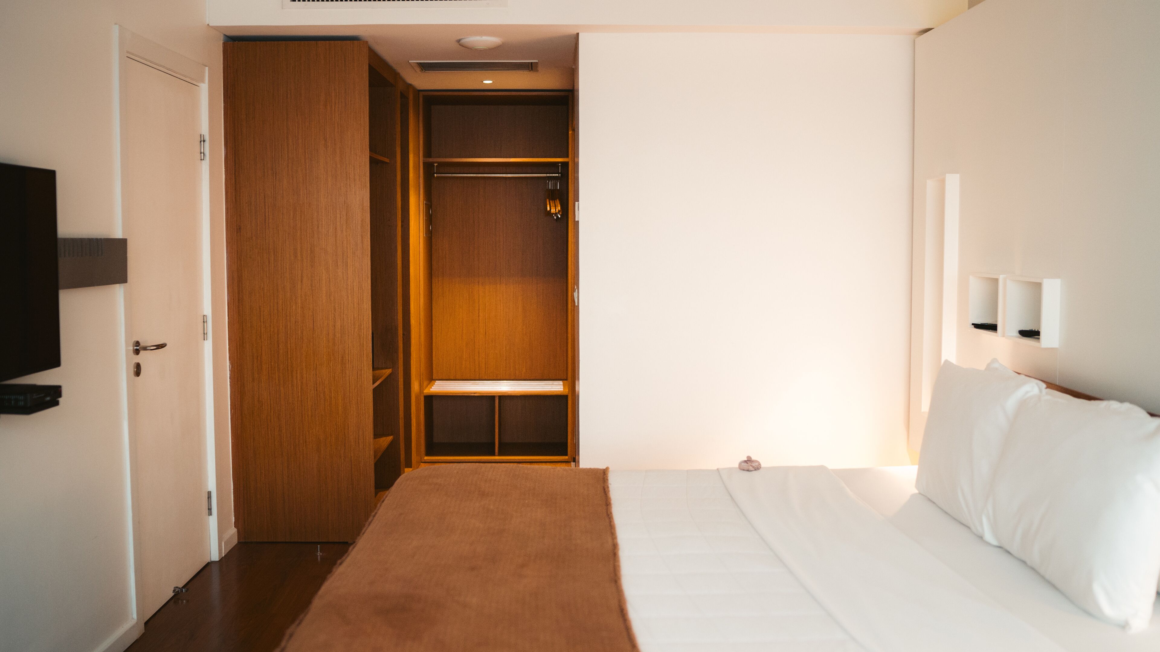 Quarto de hotel com uma cama, um guarda-roupa de madeira e uma televisão na parede.